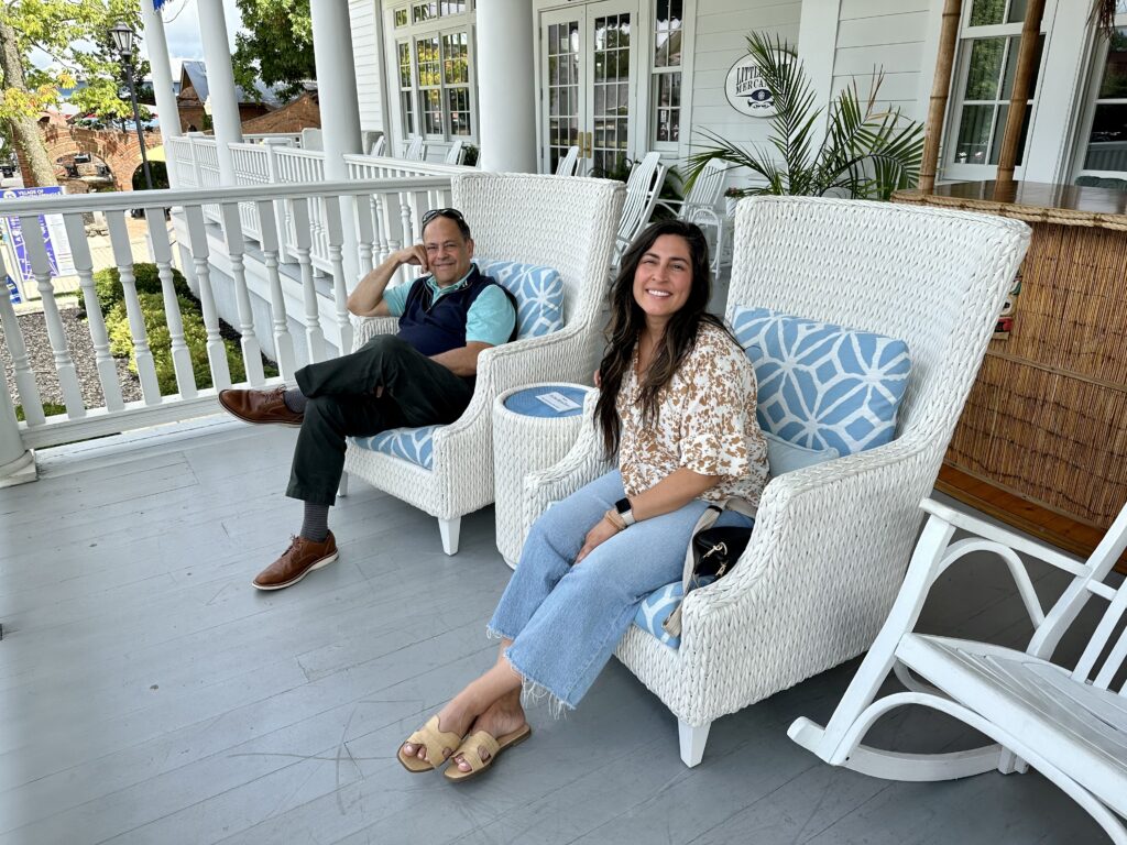 woman and man sitting in white wicker chairs on a patio with blue and white decorative pillows