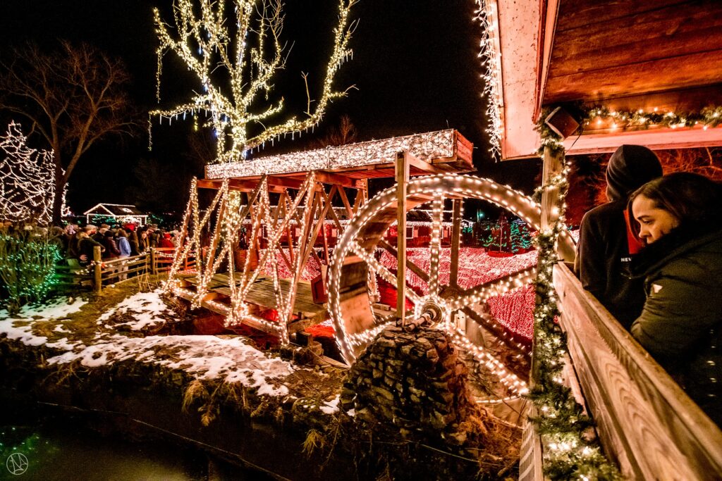 christmas lights decorating a bridge, trees, and a water mill