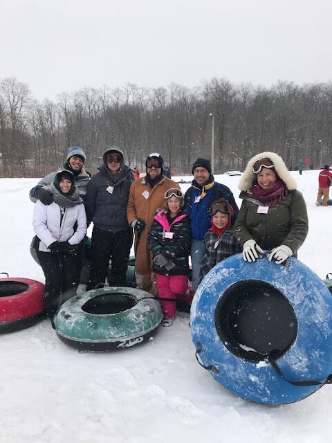 family standing on a snowy hill with innertubes for tubing down the hill