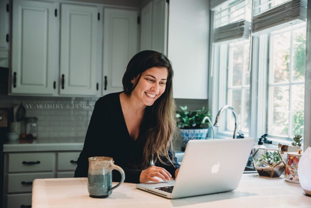 giselle sitting at a counter with her laptop in front of her, smiling with a coffee cup beside the laptop