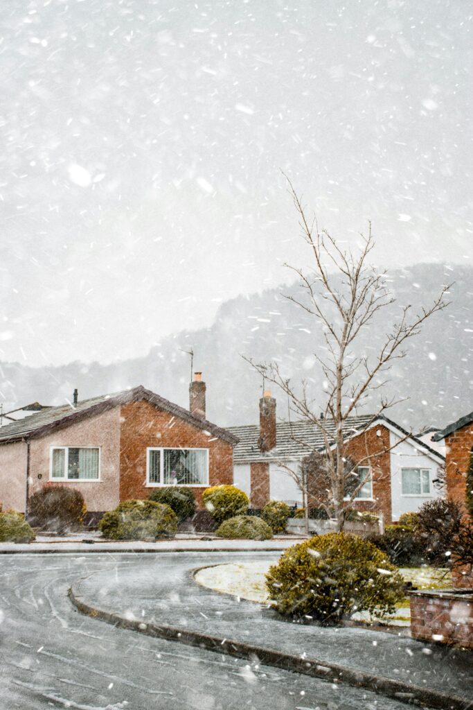 two houses side by side on a bend in the road, while it's snowing outside