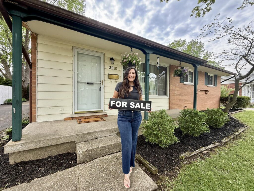 Giselle standing in front of a home holding a for sale sign
